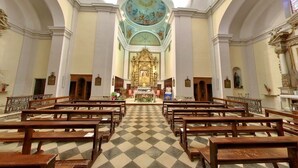 Interior de iglesia con bancos de madera dispuestos en filas, suelo a cuadros y un altar central.