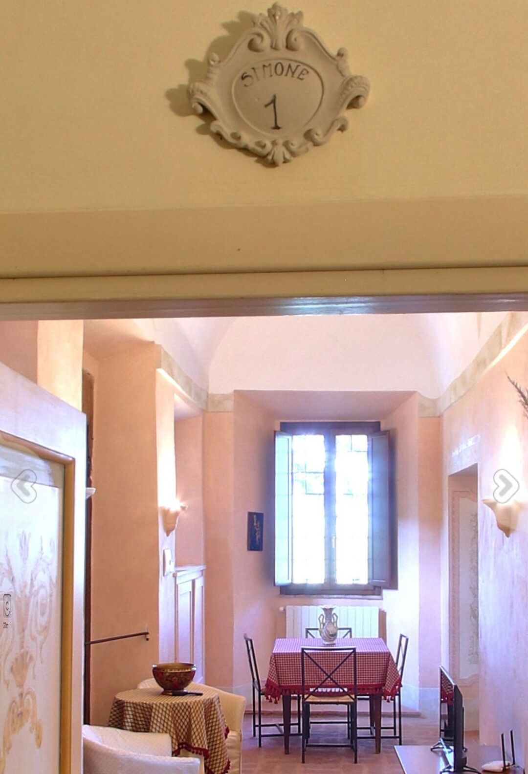 A dining area with a table set for four, a vase on the table, and a sign above the table that reads "SIMONE 1".