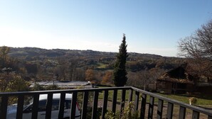 Vista desde un balcón con barandilla, que da a un valle con casas y árboles.