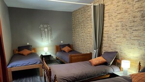Una habitación con tres camas de madera, cada una con una almohada y una mesita de noche con lámpara.