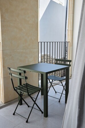 A balcony with a table and two chairs, a stone wall, and a metal railing. - Alinea Primo Historic Center  (Limassol)