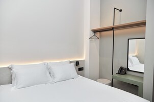 Una habitación de hotel moderna con cama, mesita de noche, lámpara de pared y espejo.