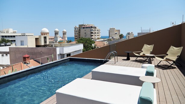 Una piscina en la azotea con sillones de descanso y vistas de la ciudad.