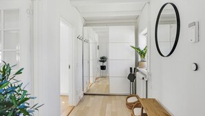Un pasillo con suelo de madera, paredes blancas, un espejo con marco negro y una planta en maceta.