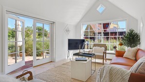 Amplia sala de estar con un gran ventanal corredizo que da a un jardín, un sofá cómodo, una mesa de centro y un televisor sobre un mueble.