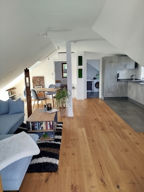 A modern loft apartment with a dining area, a living room with a sofa and coffee table, and a kitchen with grey cabinets.
