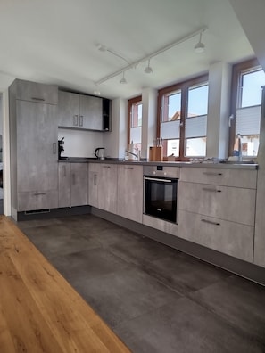 A modern kitchen with grey cabinetry, a built-in oven, and a window with blinds.