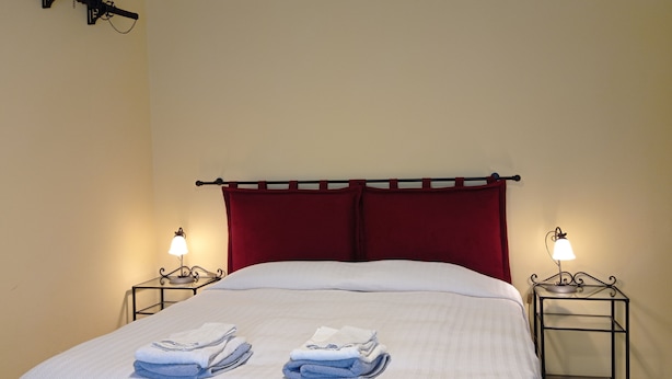 A neatly made bed with two sets of folded towels, a red headboard, and two bedside lamps on matching nightstands. - Spacious apartment with a view in the center of Montepulciano, Tuscany, Siena  (Montepulciano)