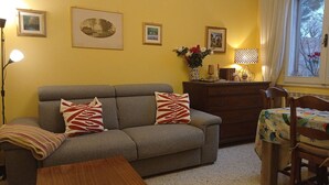 A living room with a sofa, two pillows, a wooden table, a dresser, and a window with a view. - Spacious apartment with a view in the center of Montepulciano, Tuscany, Siena  (Montepulciano)