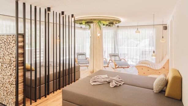 Une chambre d’hôtel moderne avec un canapé, une plante décorative, un plancher en bois et une vue sur l’extérieur.