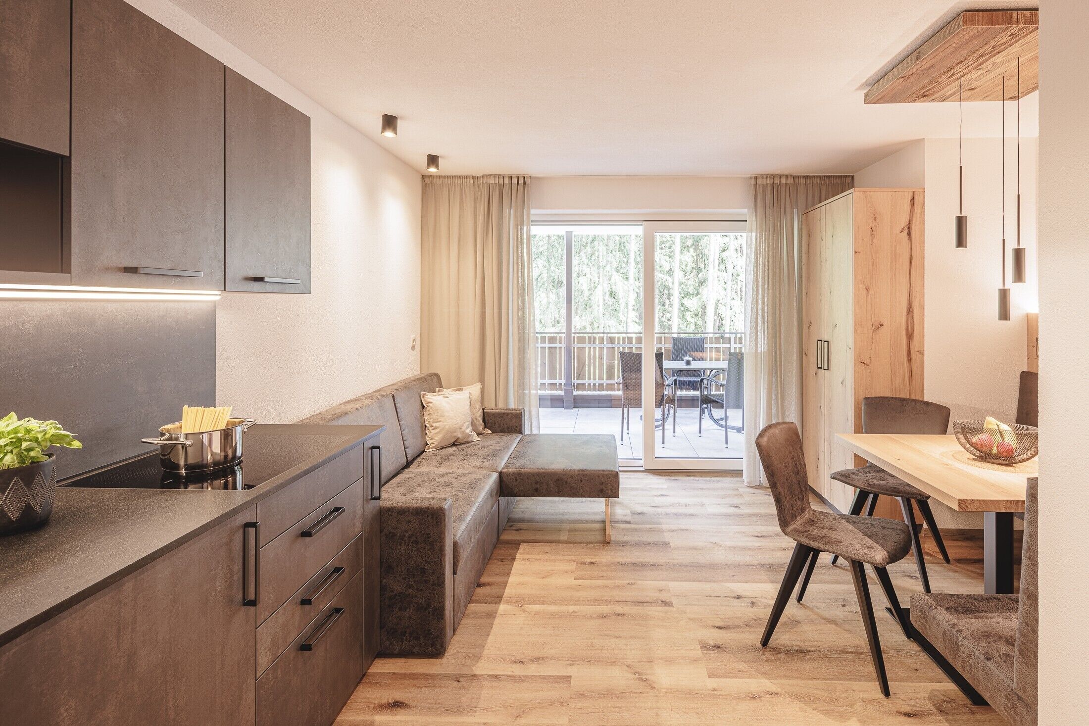 Een moderne keuken met een ingebouwde kookplaat, een eethoek met een houten tafel en stoelen, en een grote schuifpui die leidt naar een buitenbalkon.