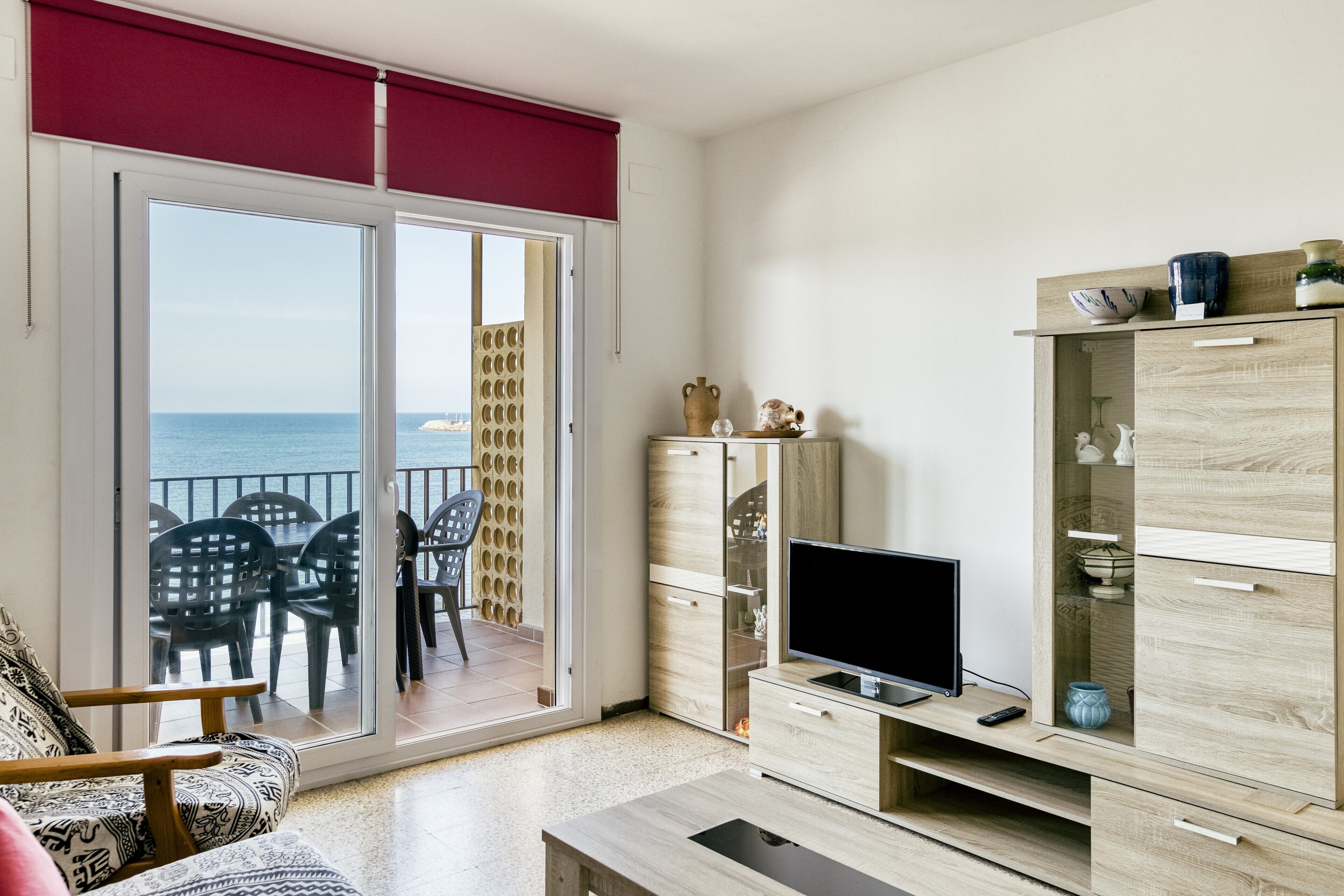 Una sala de estar con televisor, un mueble de madera y un balcón con sillas.
