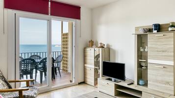 Una sala de estar con televisor, un mueble de madera y un balcón con sillas.