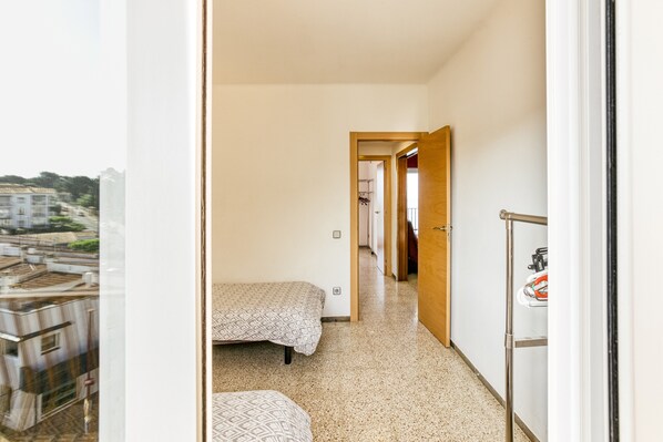 A narrow hallway with a bed and a small seating area, leading to a door.