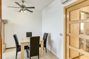 Una stanza con una ventola a soffitto, un tavolo di legno con sedie e una porta in legno.