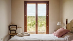 Ein Schlafzimmer mit großem Fenster, einem Bett, einem Sessel und einer Lampe.