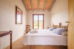 A bedroom with two beds, a wooden chair, a table, and a large window with a view.