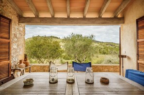 A wooden table with rustic pottery and a chair, set against a scenic hillside view.