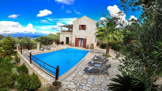 Une maison en pierre avec une piscine, entourée d’une végétation luxuriante et offrant une vue dégagée sur la mer.