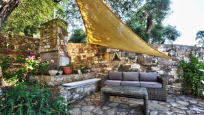 Un mur en pierre, un canapé en osier et une table dans un espace patio extérieur.