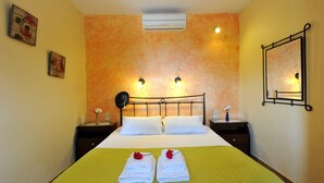 Une chambre d’hôtel comprenant un lit, deux tables de chevet, un climatiseur, des lampes fixées au mur et un miroir.