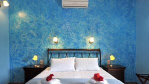 Hotelkamer met een blauwe, gestructureerde wand, een bed met witte beddengoed, twee nachtlampjes, een airconditioner en een klein tafeltje met een lamp.