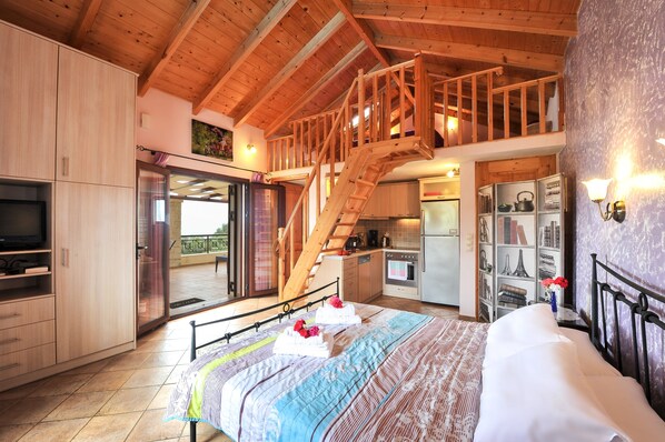 A bedroom with a bed, a wooden staircase, a kitchen, and a balcony.