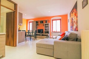 Una sala de estar moderna con un sofá gris, un comedor con mesa y sillas, y una cocina con mostrador y armarios.