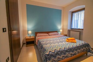 A bedroom with a bed, two bedside tables, a window, and a door. - Family apartment on the port of Castelletto - Cà Irene (Brenzone sul Garda)