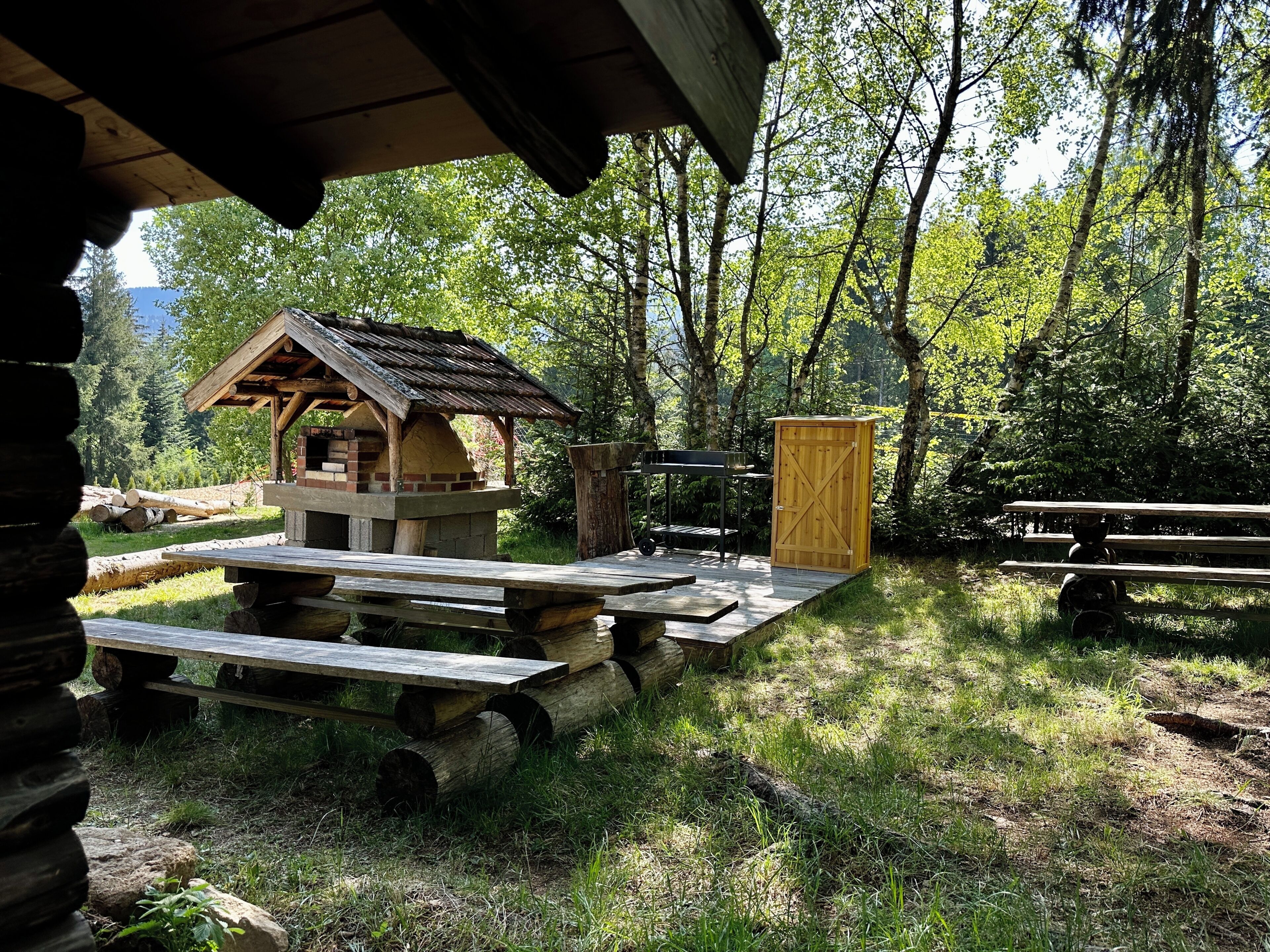 Un entorno rústico al aire libre con una estructura de madera, mesas de picnic y un cobertizo de madera.