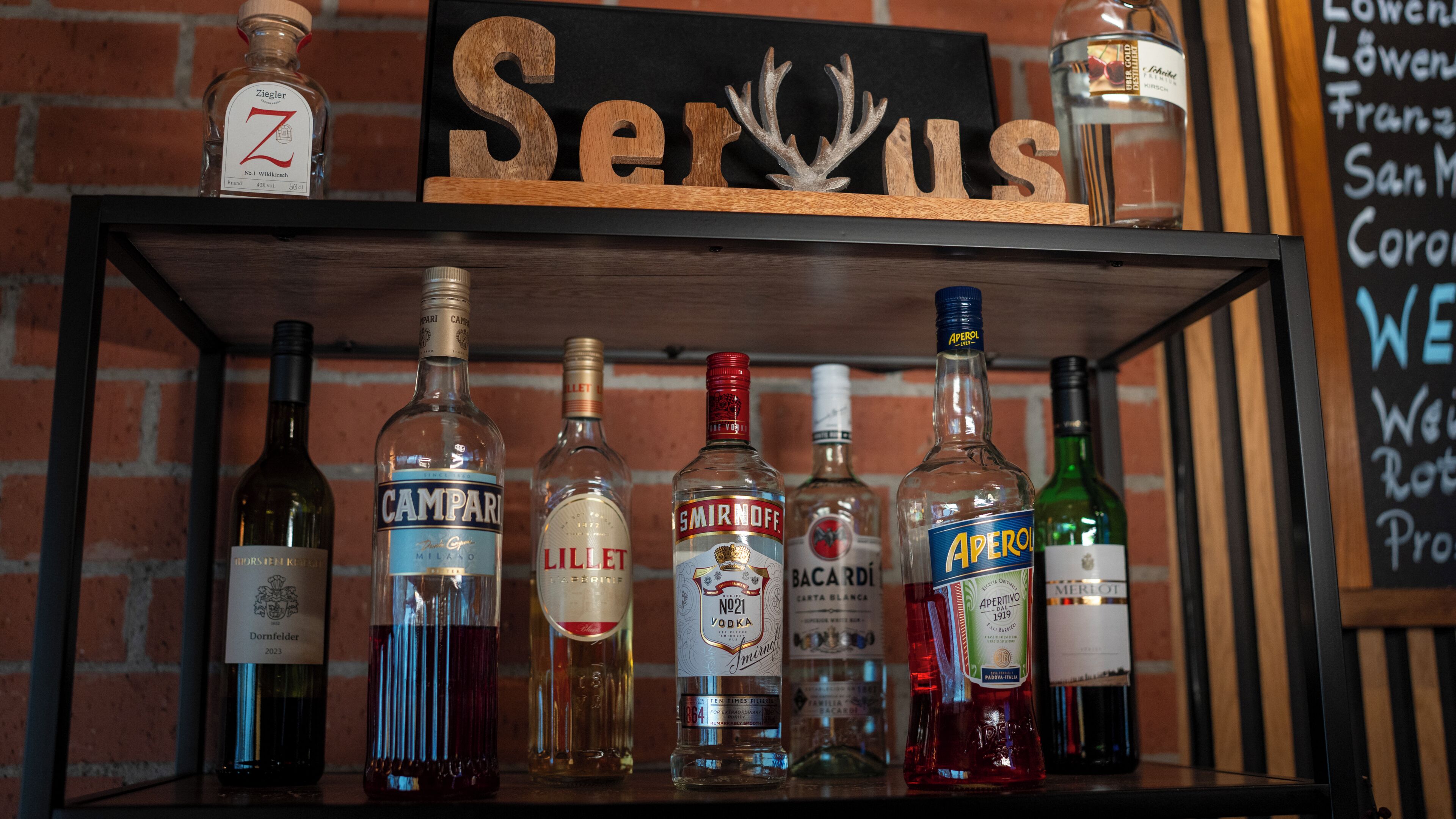 Una estantería con varias botellas de licor y un cartel que dice 'Servus'.