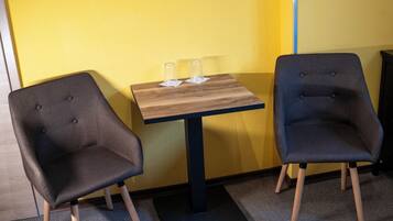 Dos sillas y una mesa con vasos, frente a una pared amarilla.
