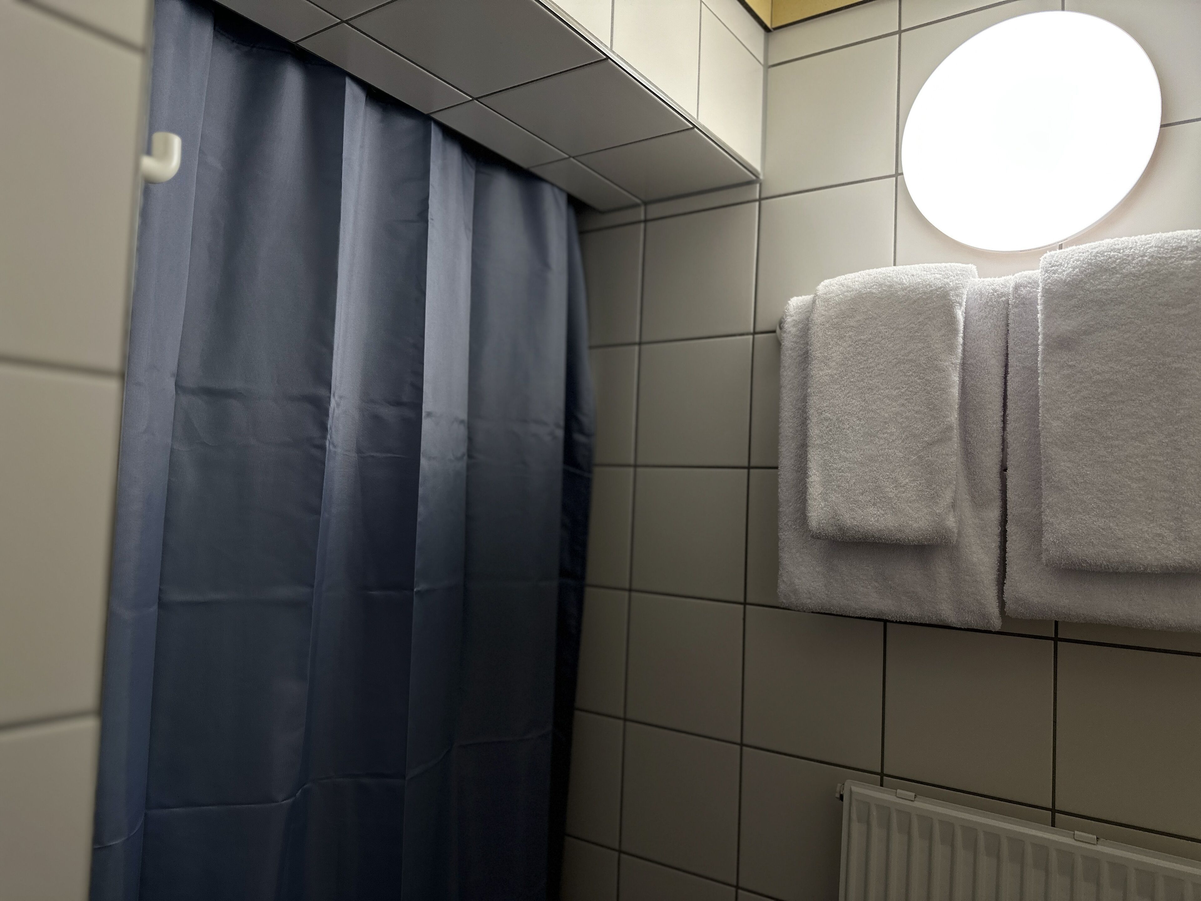 A bathroom with a blue shower curtain, a white radiator, and two white towels hanging on the wall.
