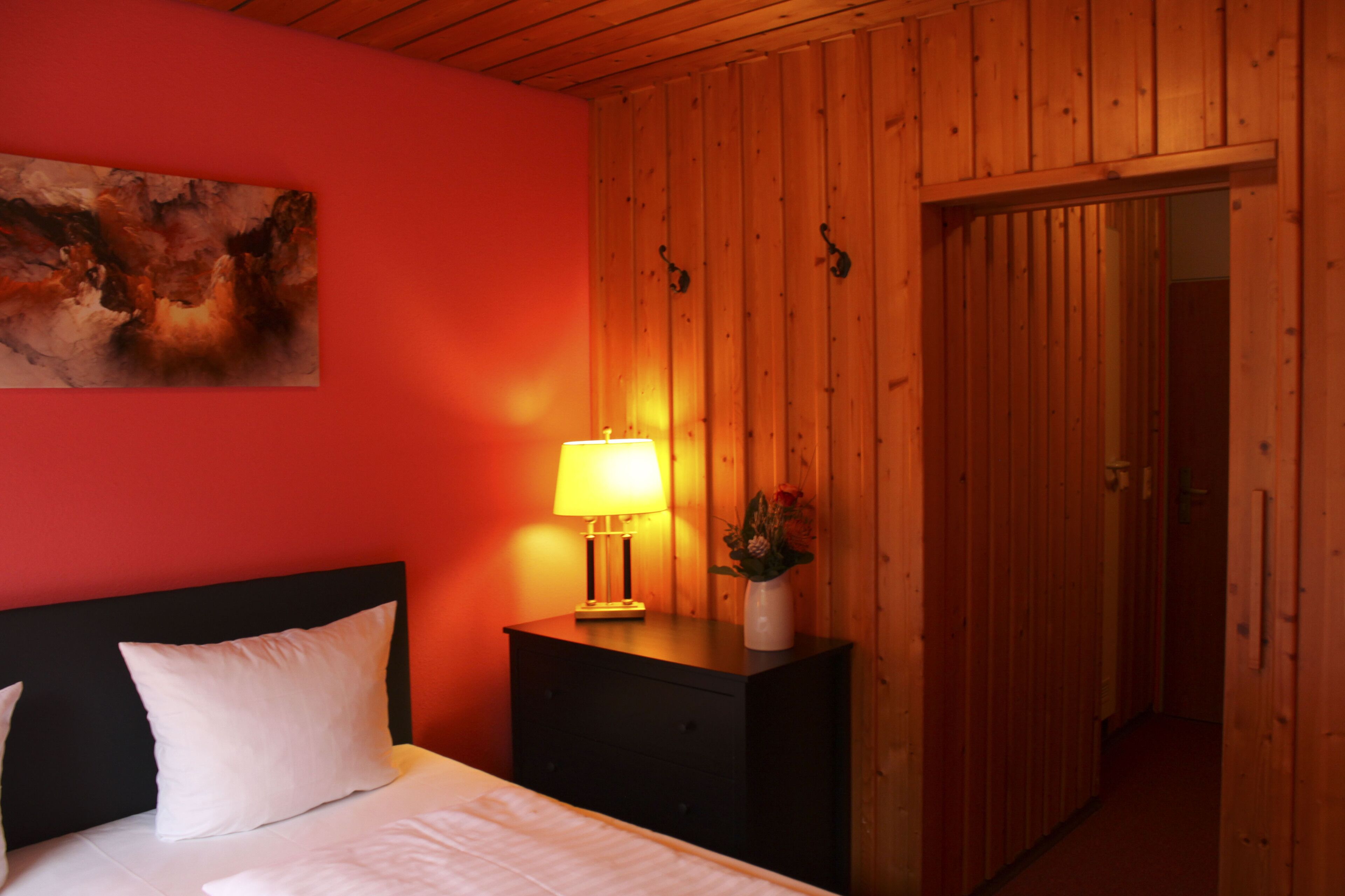 Una camera d'albergo con un letto, un comodino con una lampada, un quadro appeso e pannelli in legno.