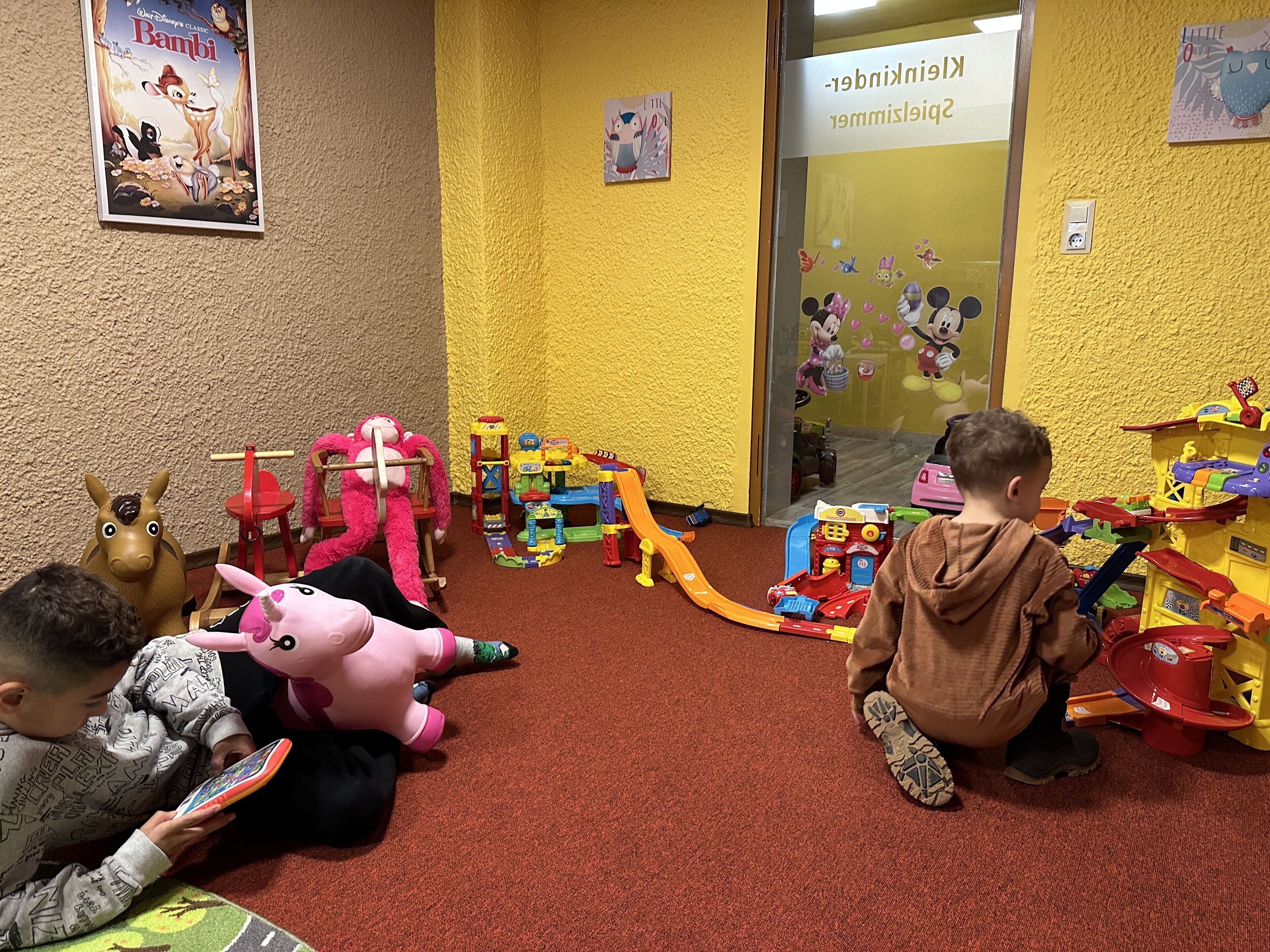 Una habitación con pared amarilla con textura, un cartel de 'Bambi' y una zona de juegos infantil con juguetes y un tobogán.