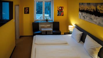A hotel room with a bed, a desk, a chair, a window, and artwork on the walls.