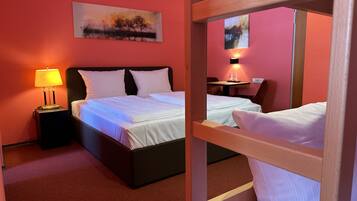 Habitación de hotel con cama, mesita de noche con lámpara, un cuadro en la pared y un espejo que refleja la habitación.