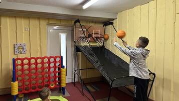 A child playing basketball in a room with a small indoor court, a red and yellow play structure, and a door labeled "Home" and "Visitor".