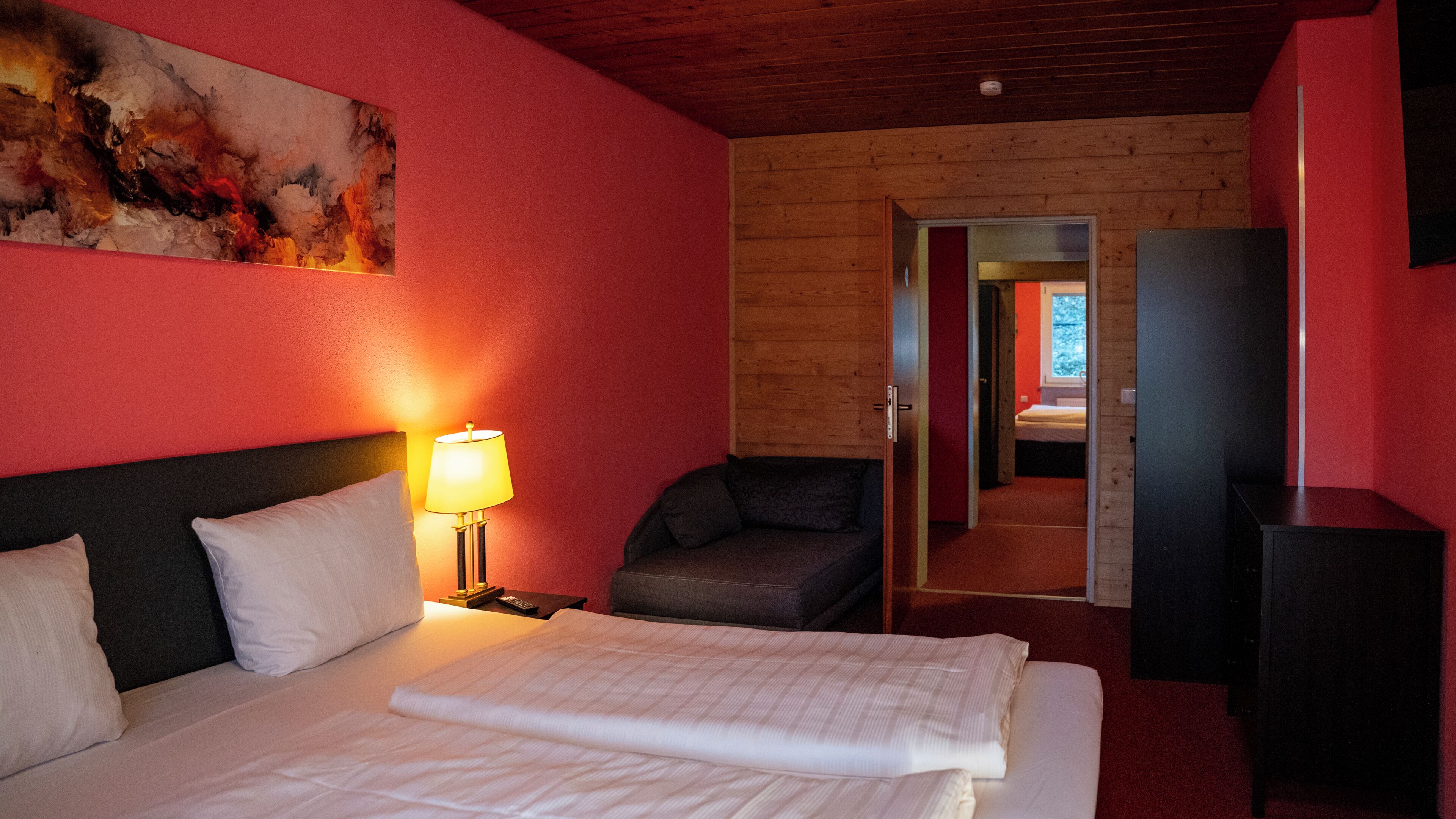 Une chambre d’hôtel avec un lit, une table de chevet, une lampe, une chaise et un tableau au mur.