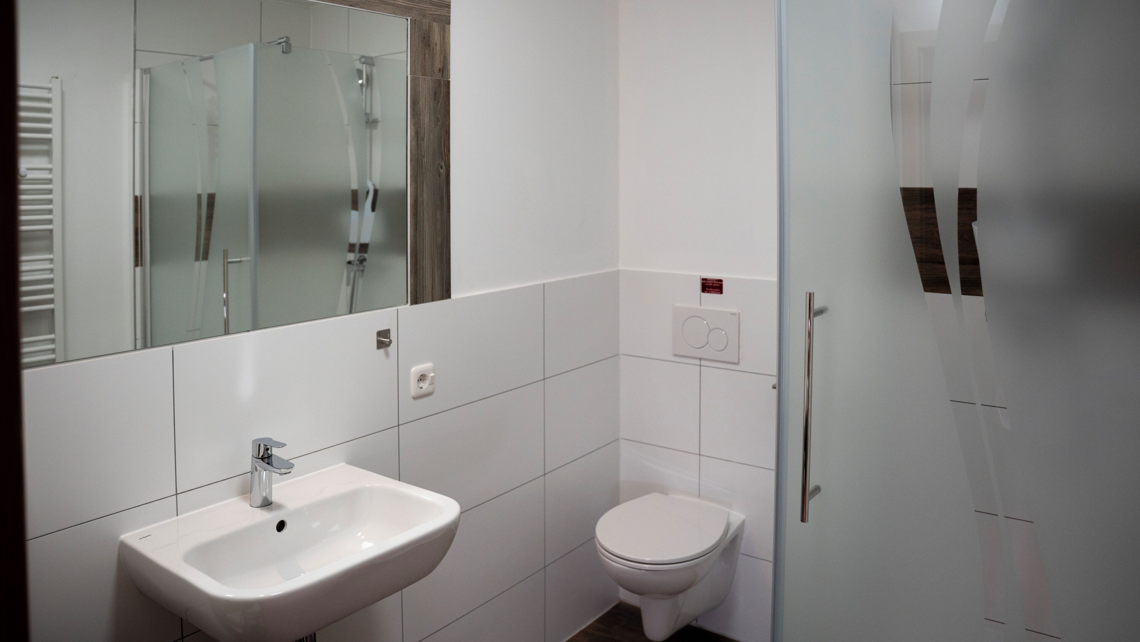 A modern bathroom with a white sink, toilet, and glass shower enclosure.