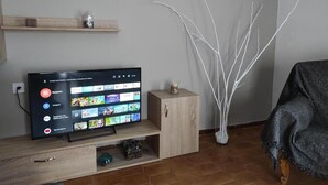 A living room with a flat-screen TV on a wooden stand, a small cabinet, a decorative vase, and a chair.