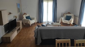 A modern hotel room with a bed, two armchairs, a TV, and a coffee table.