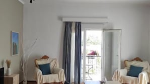 A bedroom with a bed, two chairs, a table, a TV, and a balcony with a view.