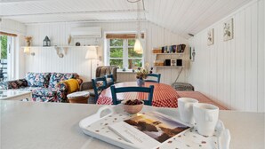 A cozy, well-lit room with a dining table set for two, a floral sofa, and a bookshelf filled with books and decorative items.