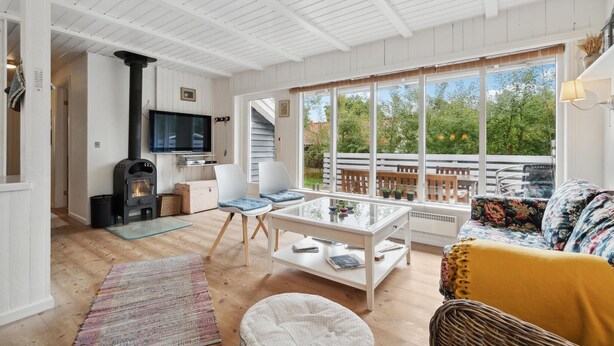 A cozy living room with a fireplace, a TV, and a large window overlooking a deck.