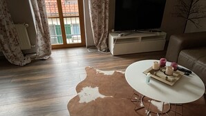 A living room with a cowhide rug, a white round table, a sofa, a TV, and a radiator. - Haus Leipheim (Leipheim)