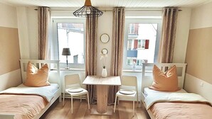 A room with two single beds, a small table, two chairs, a lamp, and a window with curtains. - Haus Leipheim (Leipheim)