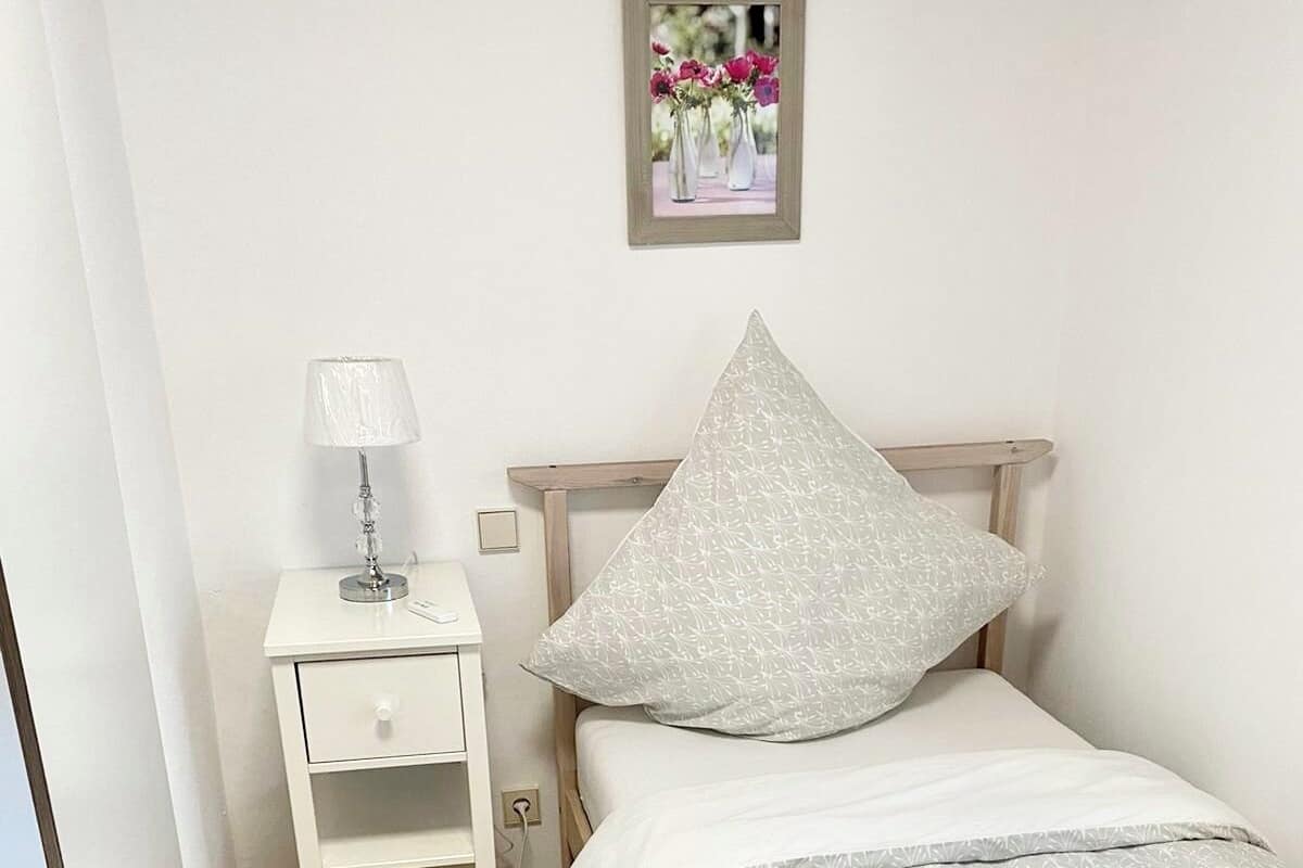 Un dormitorio con cama, mesita de noche, lámpara y un cuadro en la pared.