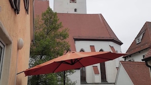 A building with a clock tower, a red umbrella, and a table with chairs. - Haus Leipheim (Leipheim)