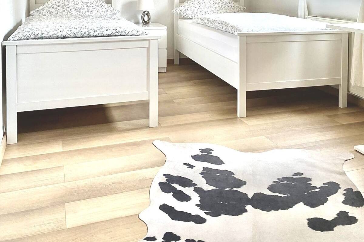 Un dormitorio con dos camas blancas, techo de madera, un cuadro de paisaje grande y una alfombra de cuero de vaca.